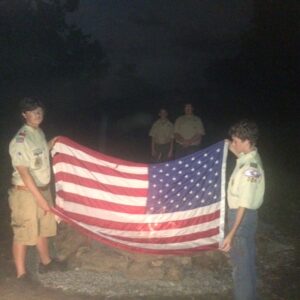 Eagle Scout Kaden Jackson on left instructing Tenderfoot Scout Joshua VandeVenter on flag retirement. First Class Scout Nick Lynam and Life Scout Nickey Cooper watch from the background.