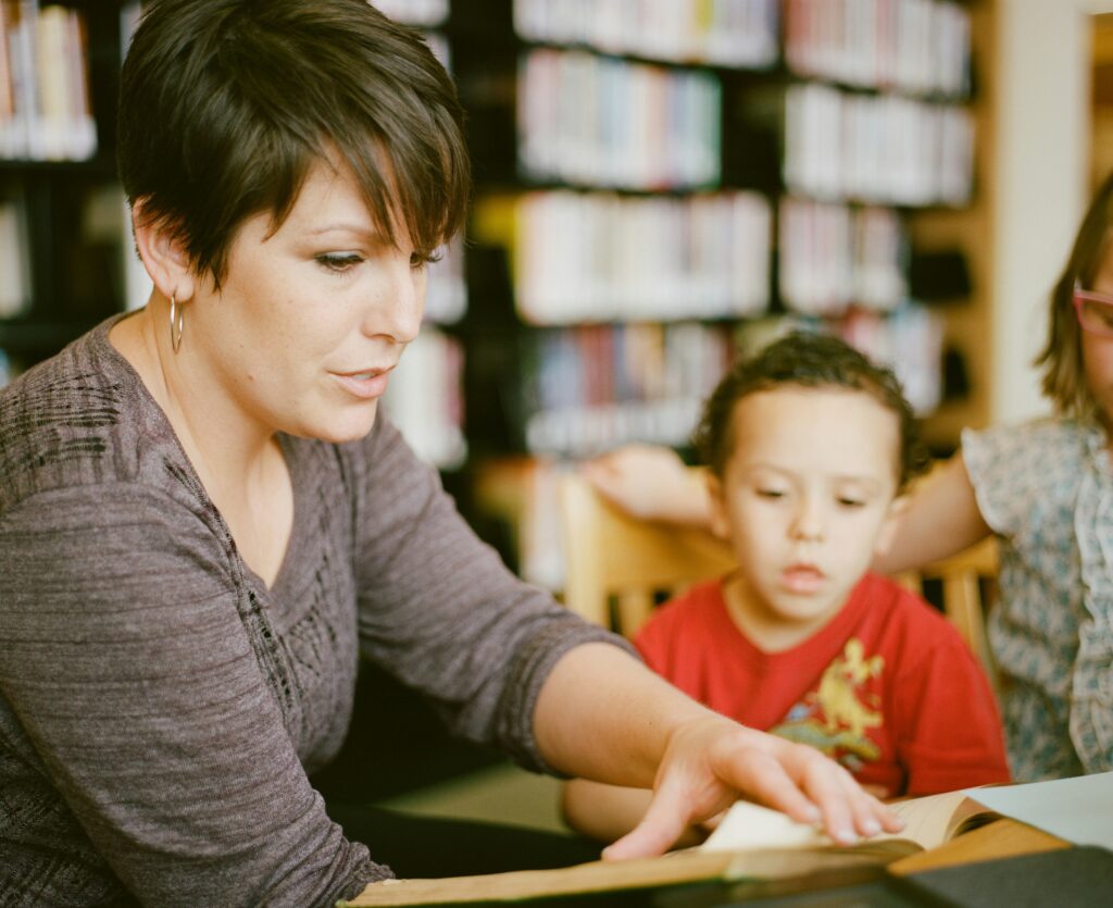 Mother reading to children inside of a library. Books in the background holding a book, kids looking and listening intently. 

https://www.instagram.com/AwCreativeUT/
https://www.awedcreative.com/
https://www.awcreativeut.com
#AwCreativeUT #awcreative #AdamWinger Adam Robert Winger