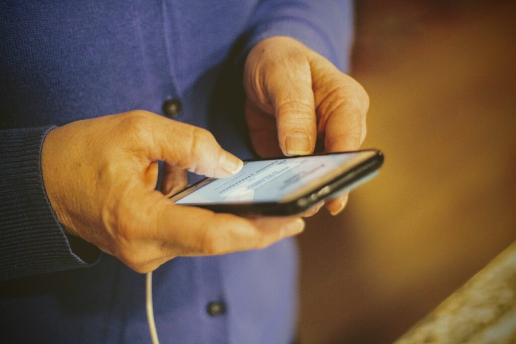 Shows a senior's hands holding an iPhone while it is charging